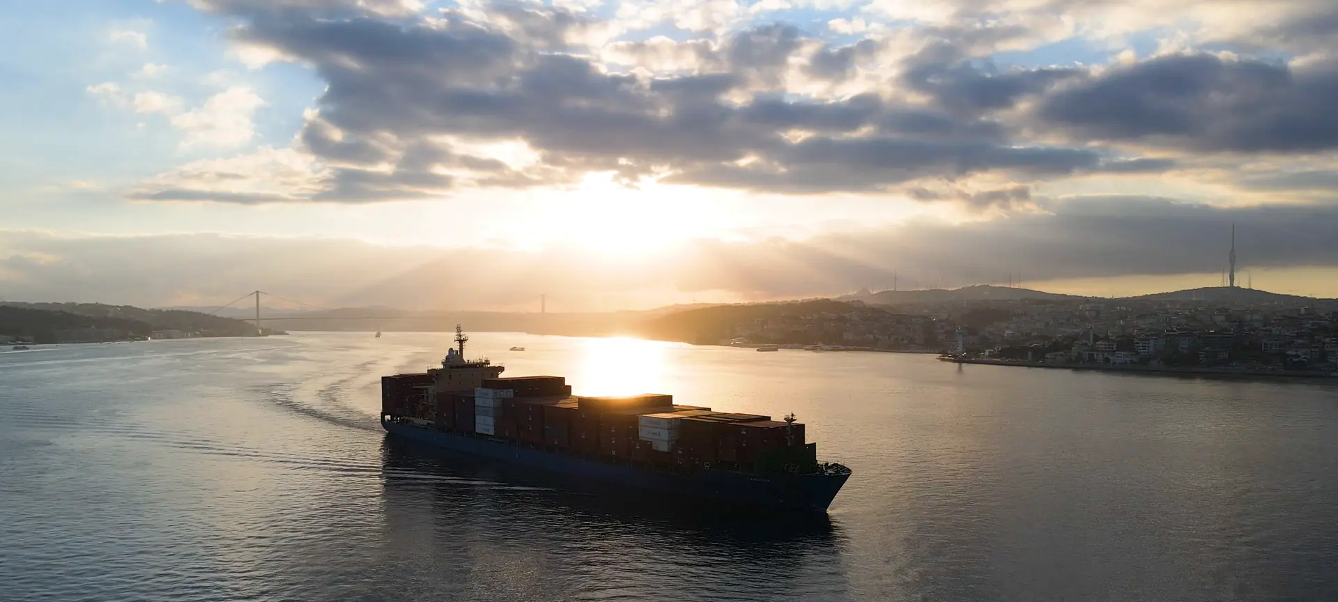 Containerschip vaart bij zonsondergang over de Bosporus, met een hangbrug op de achtergrond