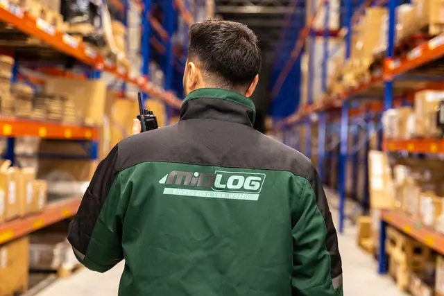 Warehousemedewerker in een groene Midlog-jas loopt tussen de stellingen