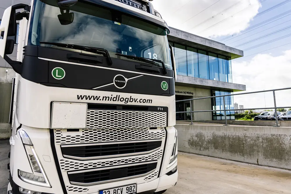 Vooraanzicht van een vrachtwagen met de website van Midlog op de grille, voor het bedrijfspand in Den Hoorn