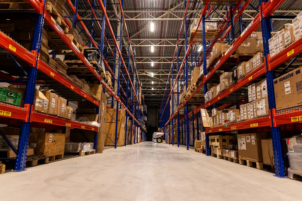 Lang gangpad tussen hoge palletstellingen met dozen en pallets in het warehouse van Midlog